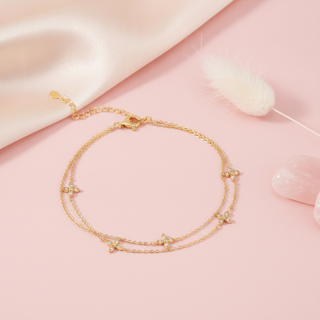 double strand gold bracelet with four-petal flower stone stations, shown on pink fabric with a dried plume