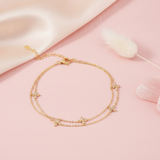 double strand gold bracelet with four-petal flower stone stations, shown on pink fabric with a dried plume