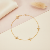 gold bracelet with three four-petal floral stone stations, shown on cream and pink fabric with a dried plume