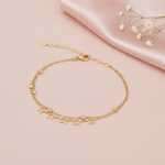 double strand gold bracelet with open star charms and small bezel-set stones, shown on pink fabric with baby's breath
