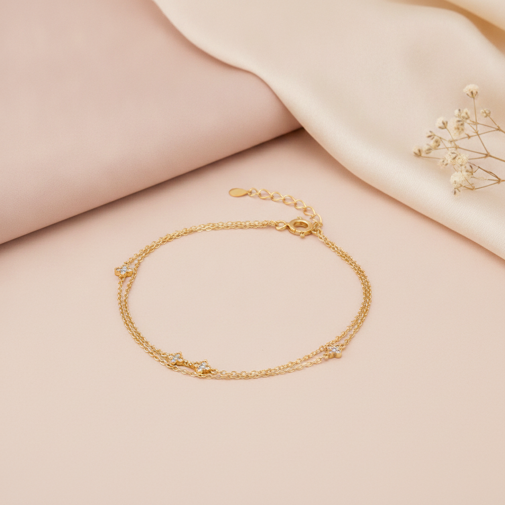 double strand gold bracelet with four-petal bloom stone stations, shown on cream fabric with a smooth stone and baby's breath