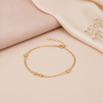 double strand gold bracelet with four-petal bloom stone stations, shown on cream fabric with a smooth stone and baby's breath