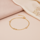 double strand gold bracelet with four-petal bloom stone stations, shown on cream fabric with a smooth stone and baby's breath