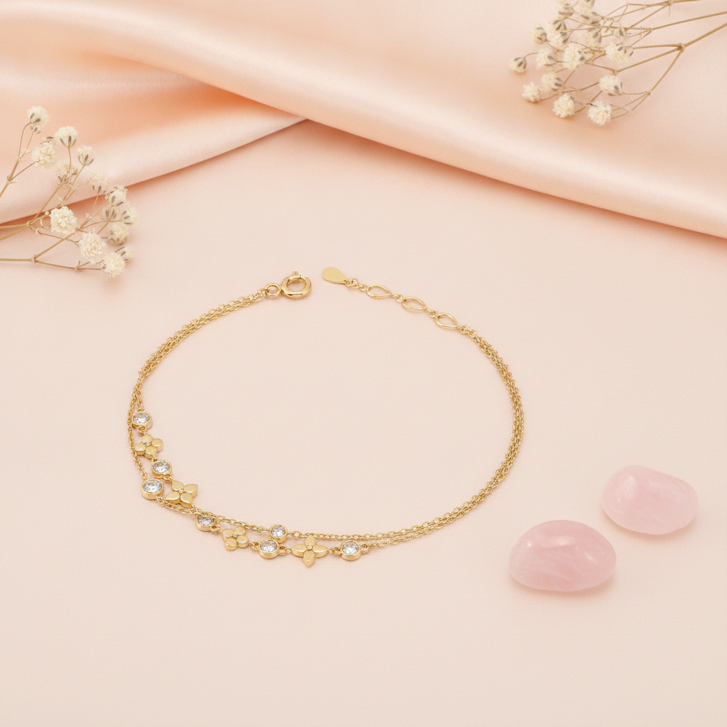 double strand gold bracelet with alternating heart and flower charm stations, shown on pink fabric with a dried rose