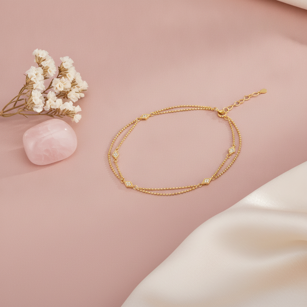 gold chain bracelet with polished cushion-shaped stone stations, shown on pink fabric with a marble dish and dried flowers