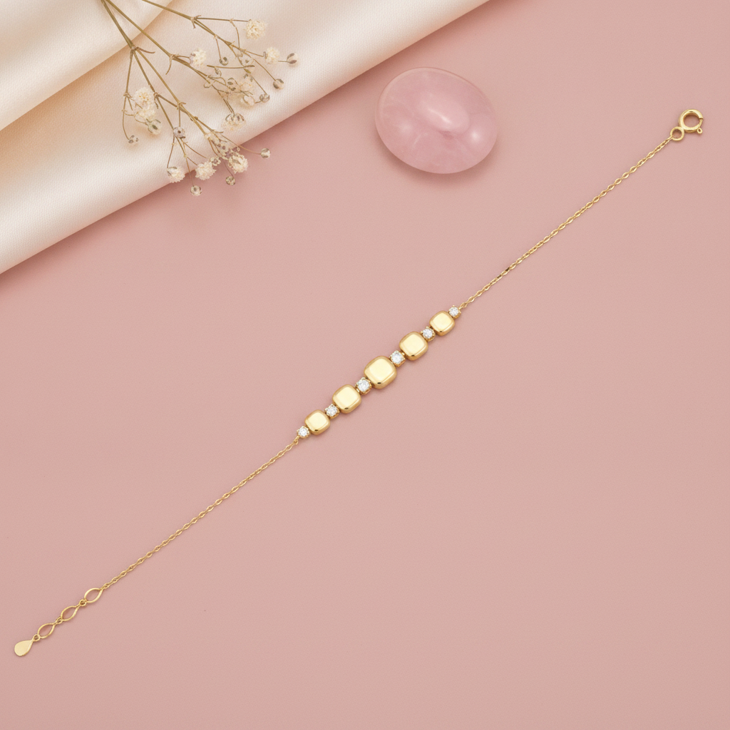 gold chain bracelet with graduated cushion-shaped stone stations, shown on pink fabric with a dried rose and a rose quartz stone