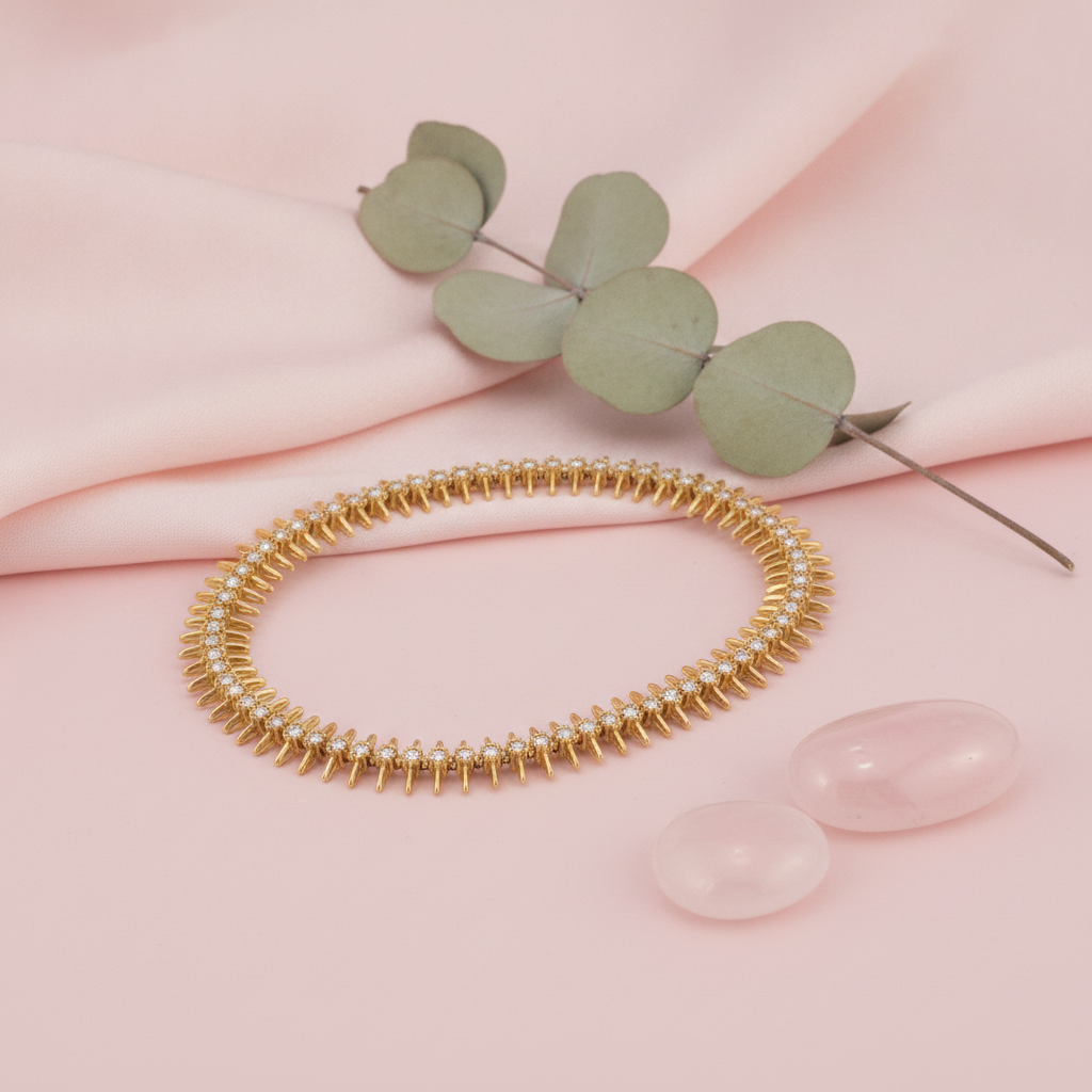 gold eternity-style bracelet with round stones framed by tapered spikes, shown on pink fabric with eucalyptus and rose quartz stones
