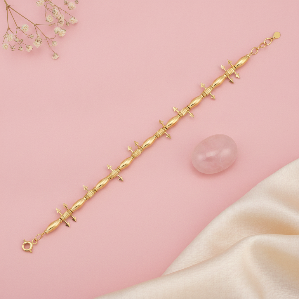 gold bracelet with alternating polished beads, textured stations, and small arrow charms, shown on pink fabric with baby's breath