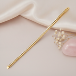 tennis-style gold bracelet with two rows of pave-set stones, shown on cream fabric with baby's breath and a rose quartz stone