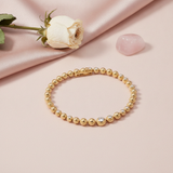 gold beaded bracelet with round beads and pave stone accents, shown on pink fabric with a dried rose and a rose quartz stone
