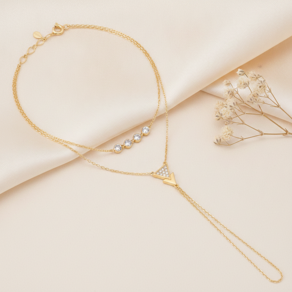 layered gold hand chain bracelet with bezel-set stones and a triangle charm, shown on cream fabric with dried baby's breath