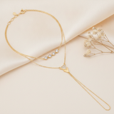 layered gold hand chain bracelet with bezel-set stones and a triangle charm, shown on cream fabric with dried baby's breath