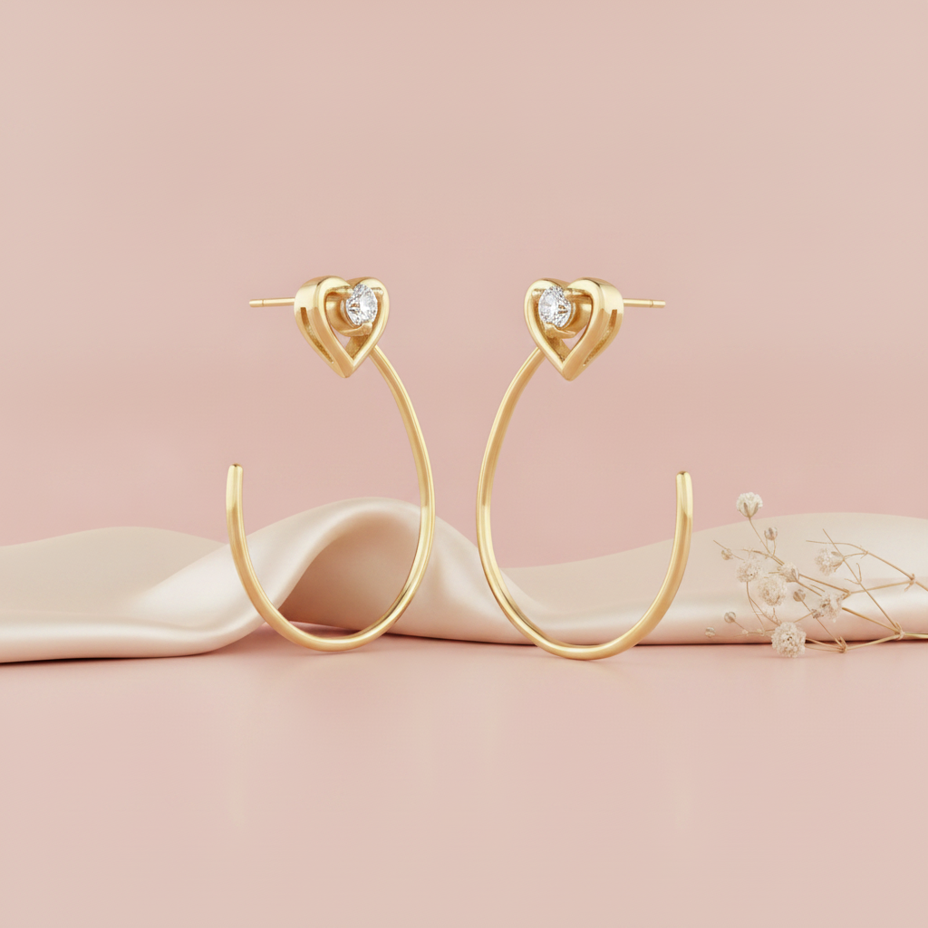 pair of gold hoop earrings topped with a heart motif and a small stone, shown on pink fabric with dried baby's breath