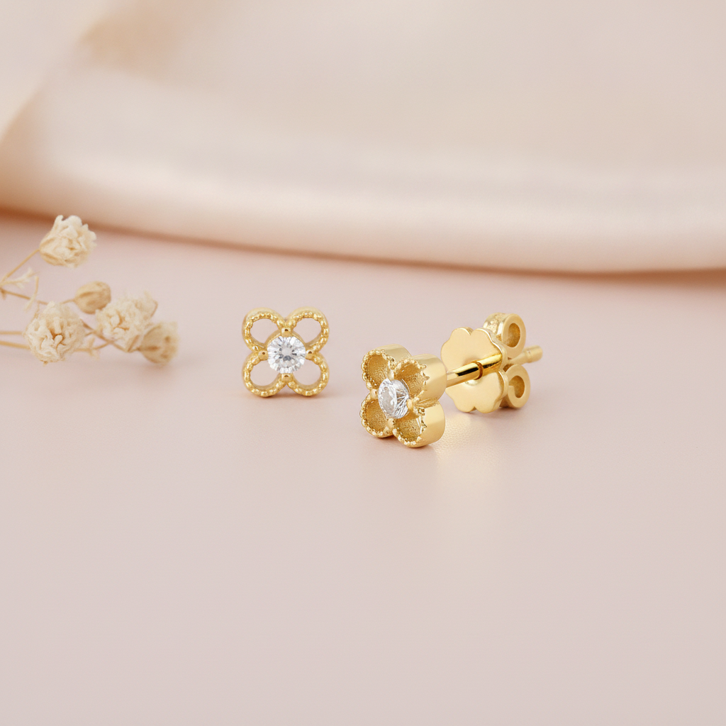 pair of four-petal openwork stud earrings with a center stone, shown front and angled on pink fabric with dried flowers