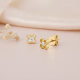 pair of four-petal openwork stud earrings with a center stone, shown front and angled on pink fabric with dried flowers