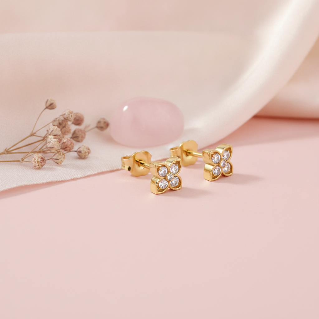 pair of four-petal floral stud earrings, shown on pink fabric with a rose quartz stone and dried flowers