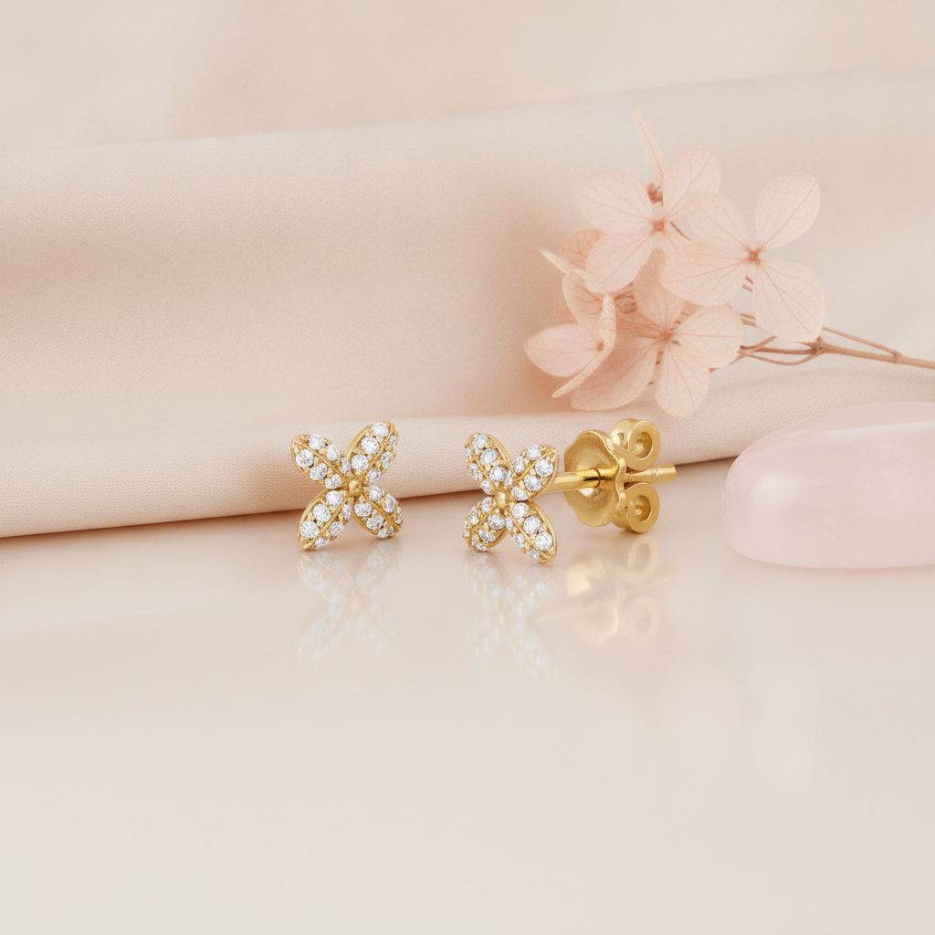 pair of X-shaped stud earrings set with clear stones, shown on cream fabric with pink dried flowers and a rose quartz stone