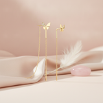 pair of butterfly threader earrings with dangling chains, shown on pink fabric with a feather and a rose quartz stone