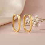 polished gold elongated oval hoop earrings on a blush background with cream satin fabric and a rose quartz stone