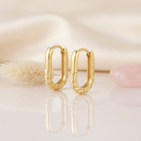 polished gold oval hoop earrings with a sculpted rope-twist base on a cream satin background with dried grass