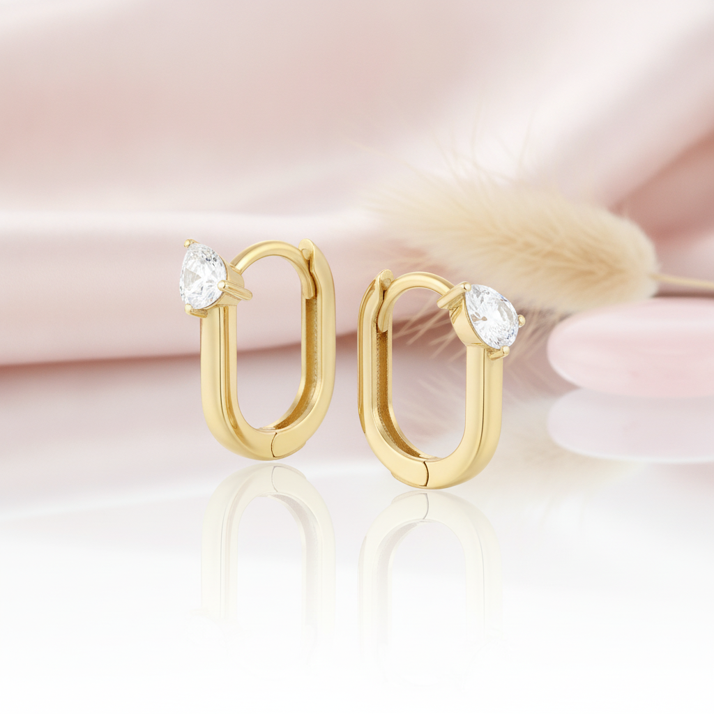 gold oval hoop earrings with a single pear-cut stone on a pink satin background with dried grass
