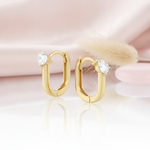 gold oval hoop earrings with a single pear-cut stone on a pink satin background with dried grass