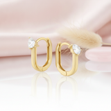 gold oval hoop earrings with a single pear-cut stone on a pink satin background with dried grass