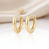 polished solid gold tapered hoop earrings on a cream satin background with a reflective white surface