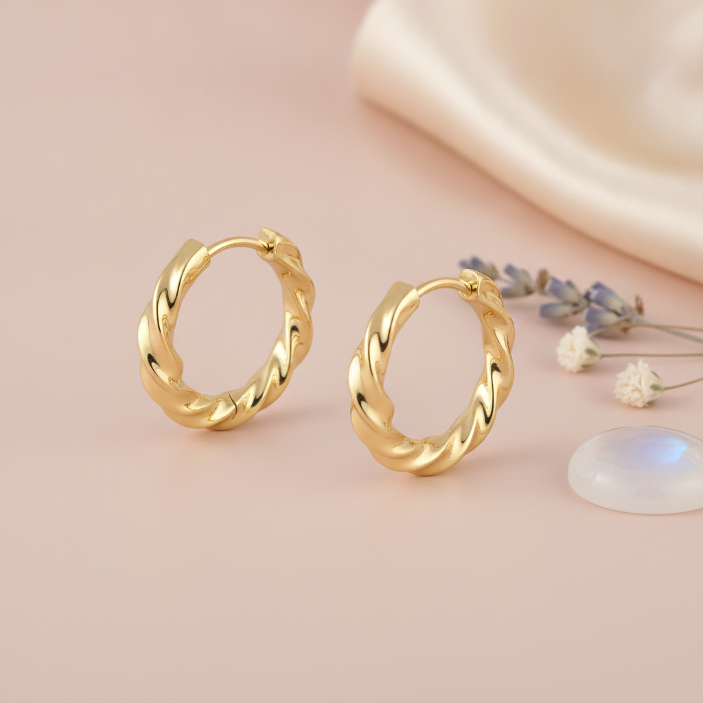 polished gold twisted huggie hoop earrings on a blush background with lavender sprigs and a translucent stone