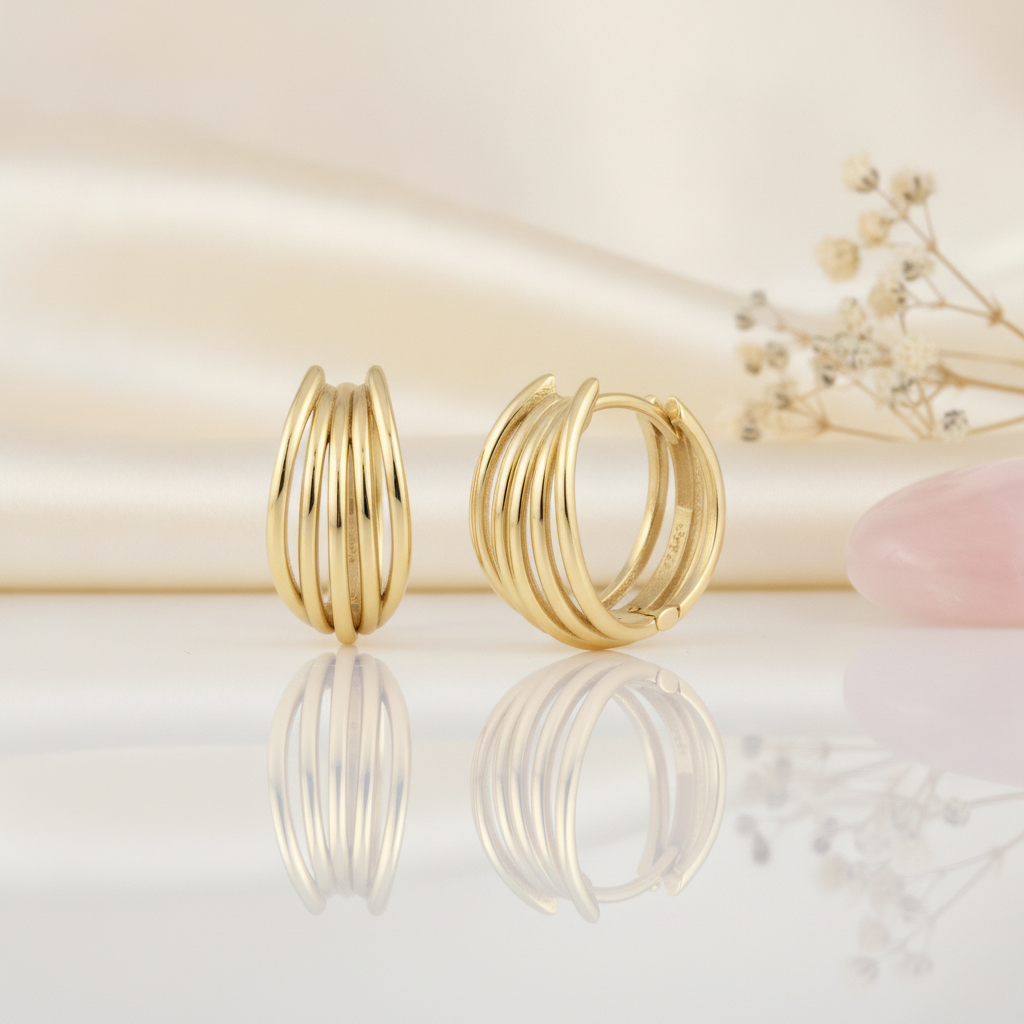 gold multi-strand arc huggie hoop earrings on a cream satin background with dried baby's breath and a rose quartz stone