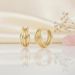 gold multi-strand arc huggie hoop earrings on a cream satin background with dried baby's breath and a rose quartz stone