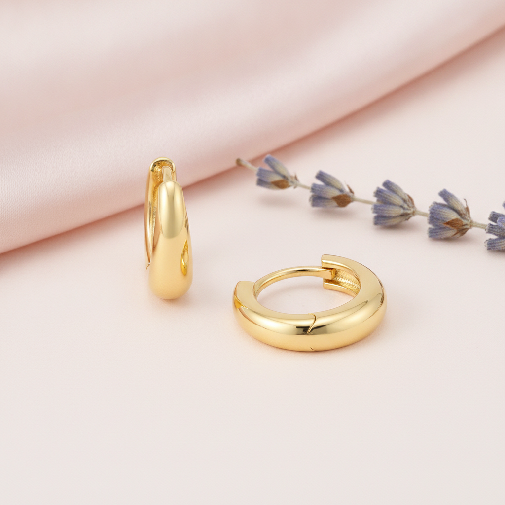 polished gold tapered huggie hoop earrings on a pink satin background with lavender sprigs