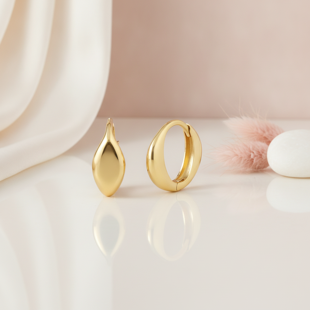 polished gold teardrop stud and curved huggie hoop earrings on a cream and blush background with a pink pebble