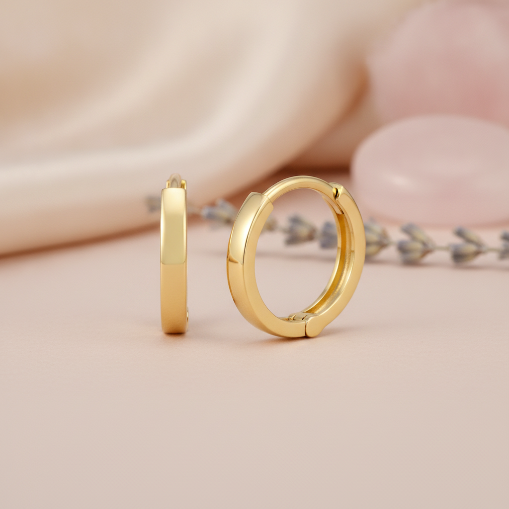 polished yellow gold flat-edge huggie hoop earrings on a blush background with a rose quartz stone and lavender sprig