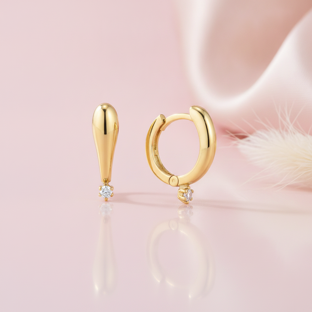 gold tapered drop earring and huggie hoop with a single round White CZ stone on a pink satin background with dried grass