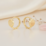solid gold huggie hoop earrings with a smooth polished disk front on a beige background with dried baby's breath
