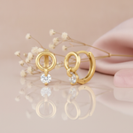 gold huggie hoop earrings with an open circle and a suspended round White CZ stone drop on a blush background with dried baby's breath