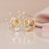 gold huggie hoop earrings with an open circle and a suspended round White CZ stone drop on a blush background with dried baby's breath