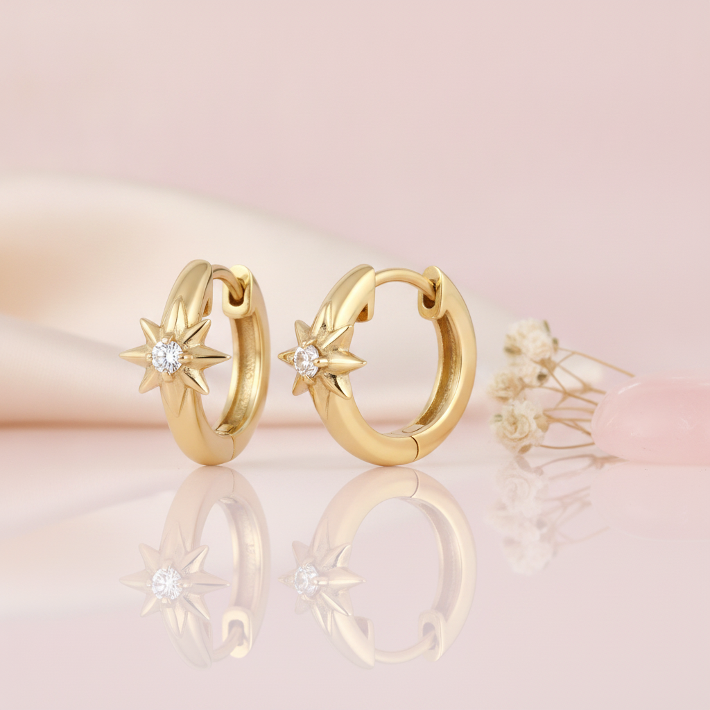 gold huggie hoop earrings with a sculpted eight-pointed star and a round White CZ stone on a blush background with dried baby's breath