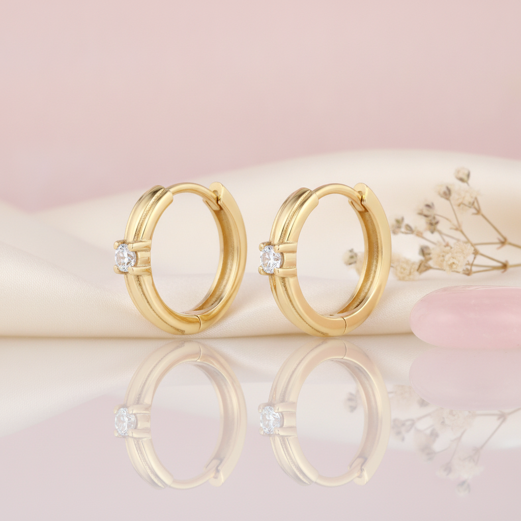 polished gold huggie hoop earrings with a single round White CZ stone on a blush background with dried baby's breath
