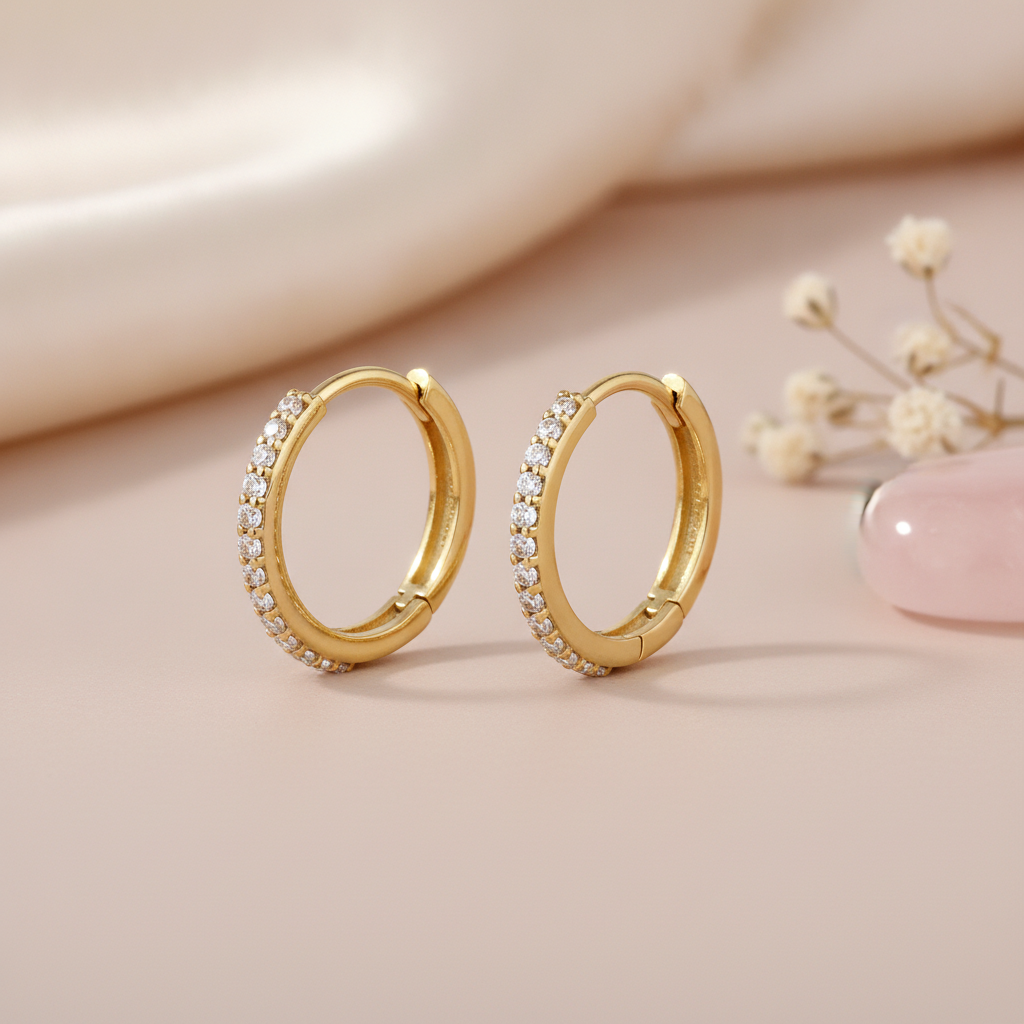 gold hoop earrings lined with a row of brilliant clear stones on a blush background with dried baby's breath and a rose quartz stone