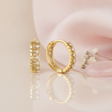 gold huggie hoop earrings with round White CZ stones and a notched openwork profile on a blush background with dried baby's breath