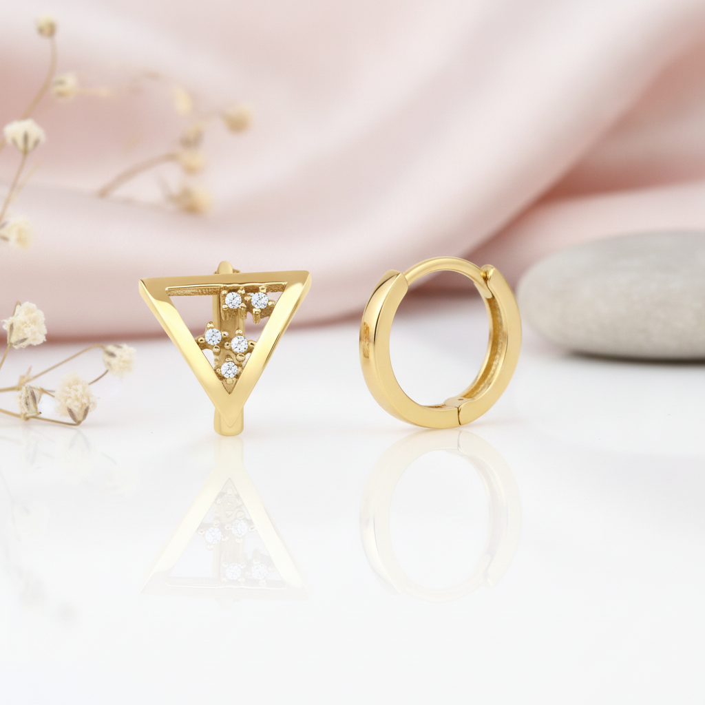 gold huggie hoop earrings with an inverted triangle charm set with five White CZ stones on a blush background with dried flowers and a gray stone