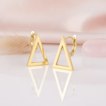 polished gold open-triangle earrings with a sharp tapering point on a blush background with dried grass and a rose quartz stone