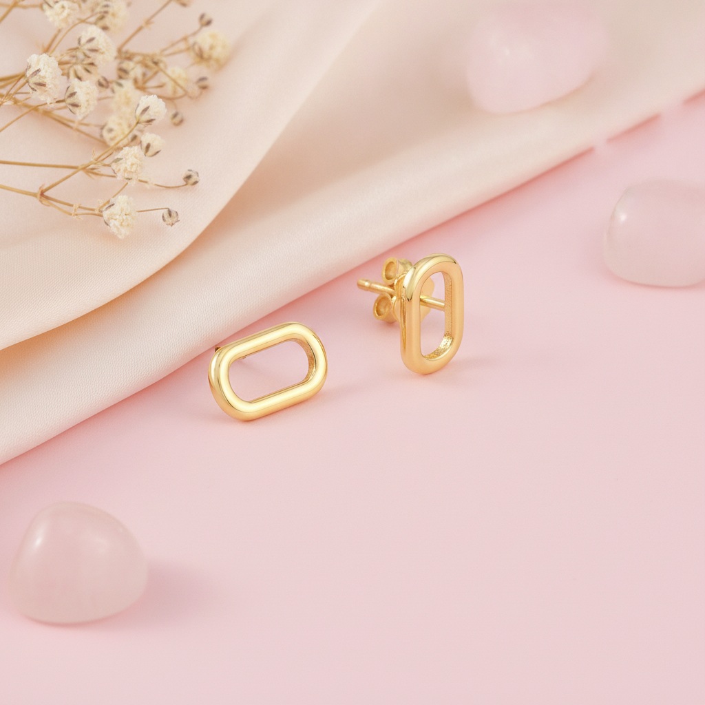 polished gold open oval stud earrings on a pink background with dried baby's breath and rose quartz pebbles