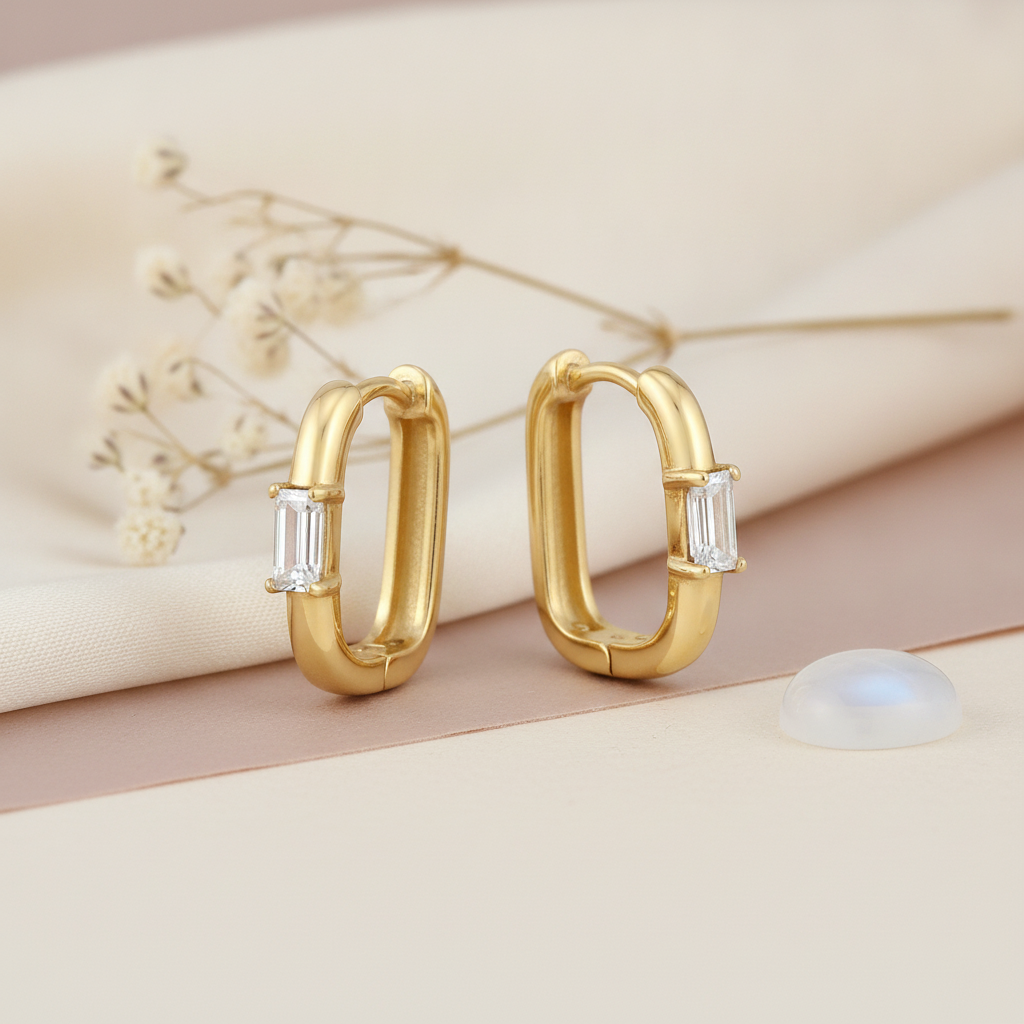 gold huggie hoop earrings with a single vertical baguette-cut White CZ stone on a cream background with a moonstone cabochon