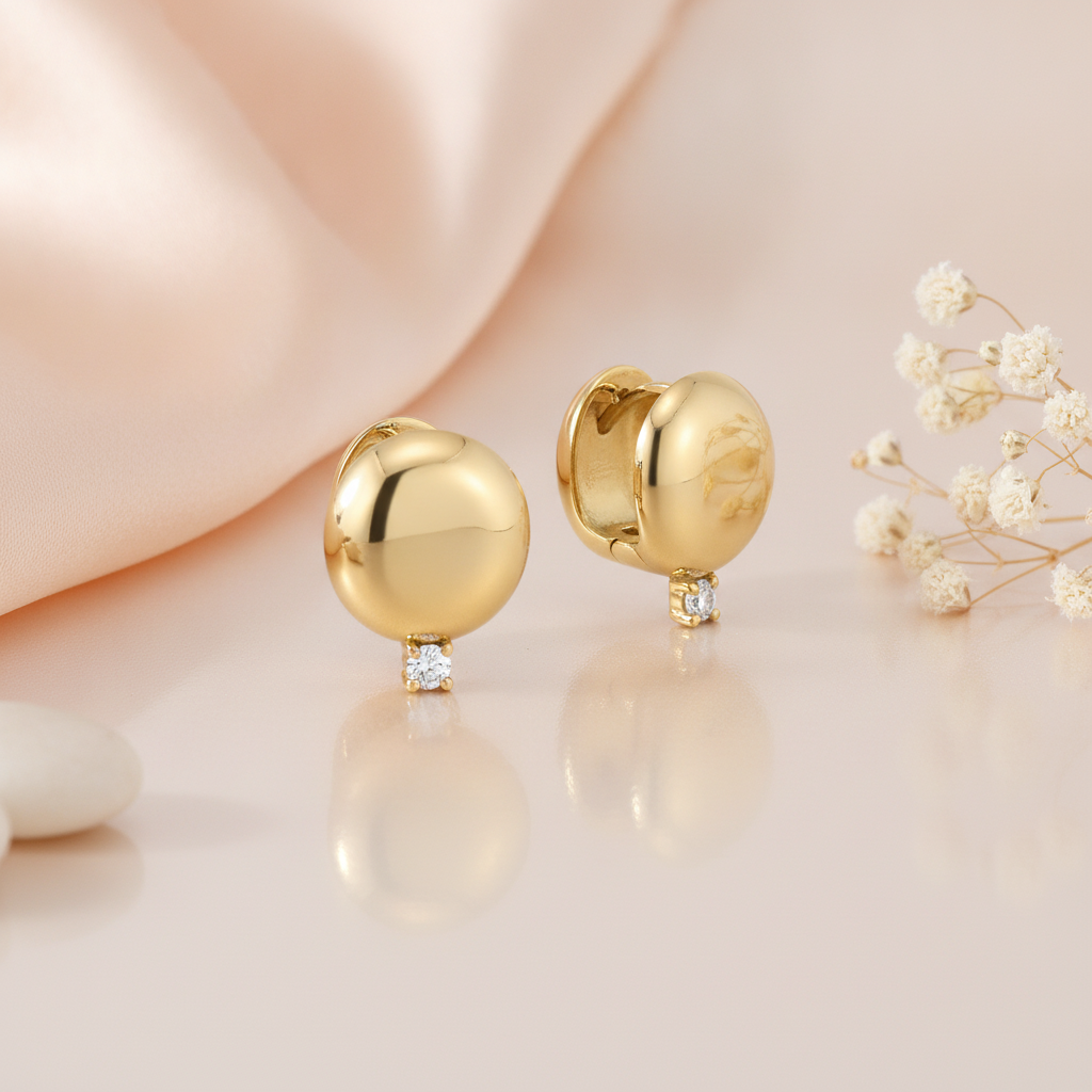 polished gold dome huggie hoop earrings with a single clear stone, styled on a blush pink background with draped silk and dried white flowers