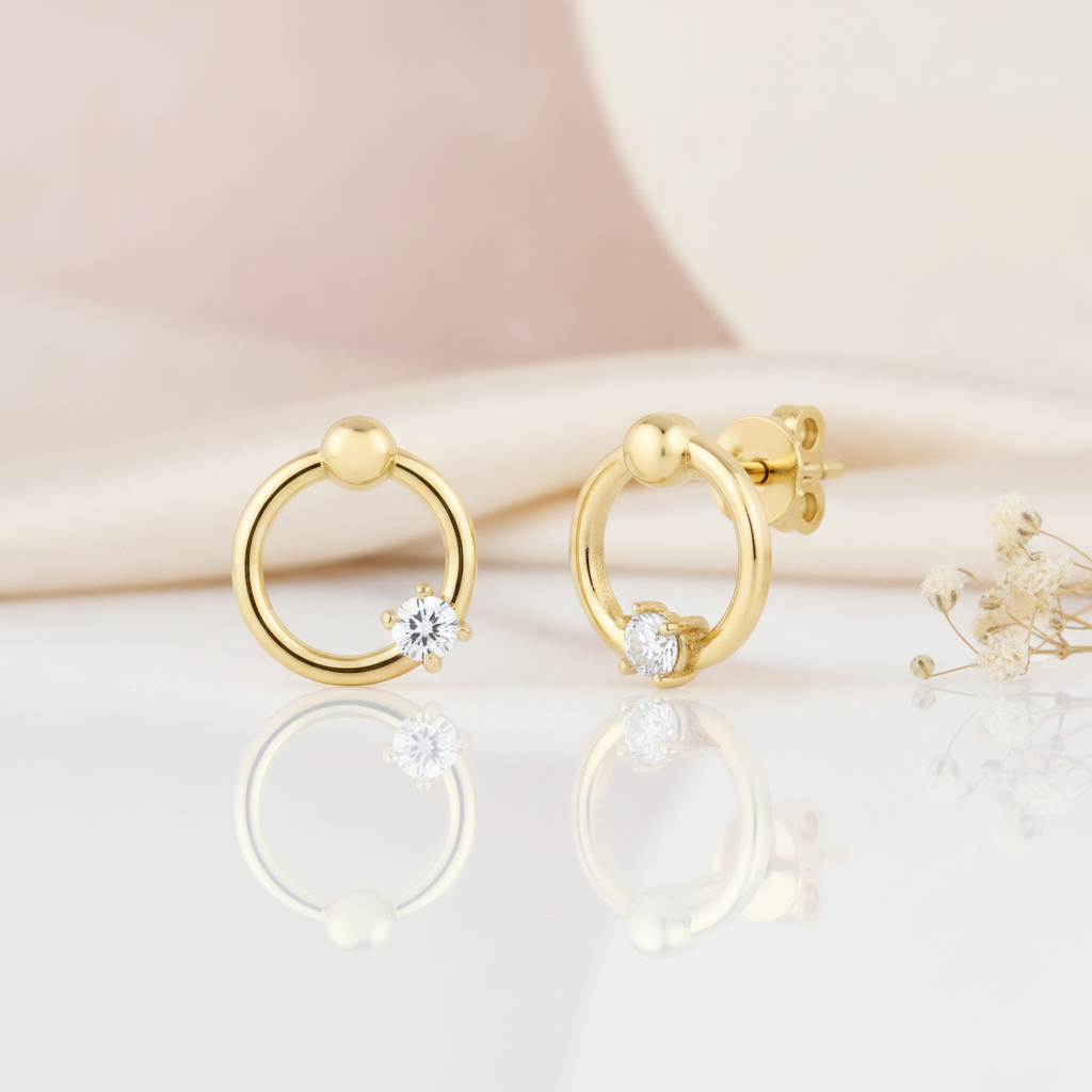 open gold ring stud earrings with a polished bead and a single clear stone, styled on a blush background with draped silk and dried flowers