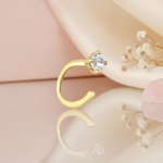 open curve gold stud earrings with a single clear stone at the tip, styled on a pink background with draped silk and dried flowers