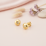 gold dome stud earrings etched with a star and set with a single clear stone, styled on a pink background with dried grass and purple statice flowers